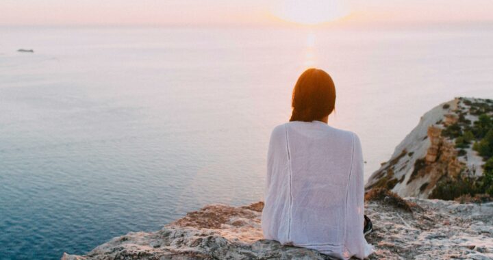 Woman Sitting on Gray Rock Near Body of Water