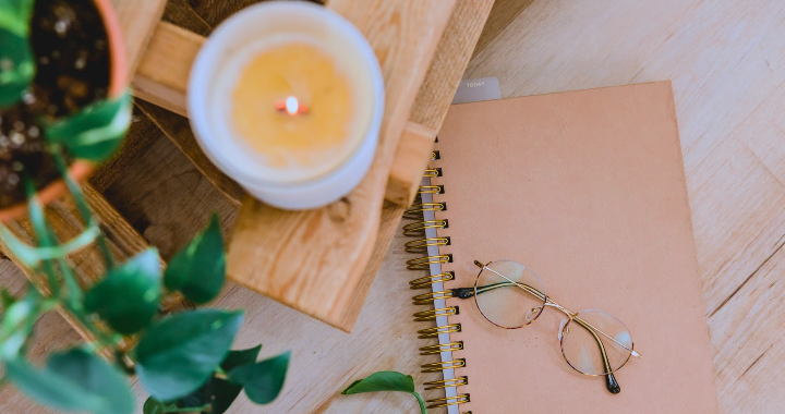 Wooden bedside tray with a candle, plant, glasses, and journal for a calming bedtime routine to recall your energy