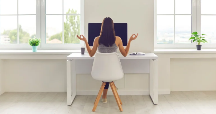 Woman practicing midday mindfulness at her office table with a computer and coffee, taking a mindful break from work